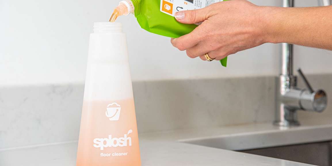 Splosh floor cleaner bottle being refilled with an orange liquid.